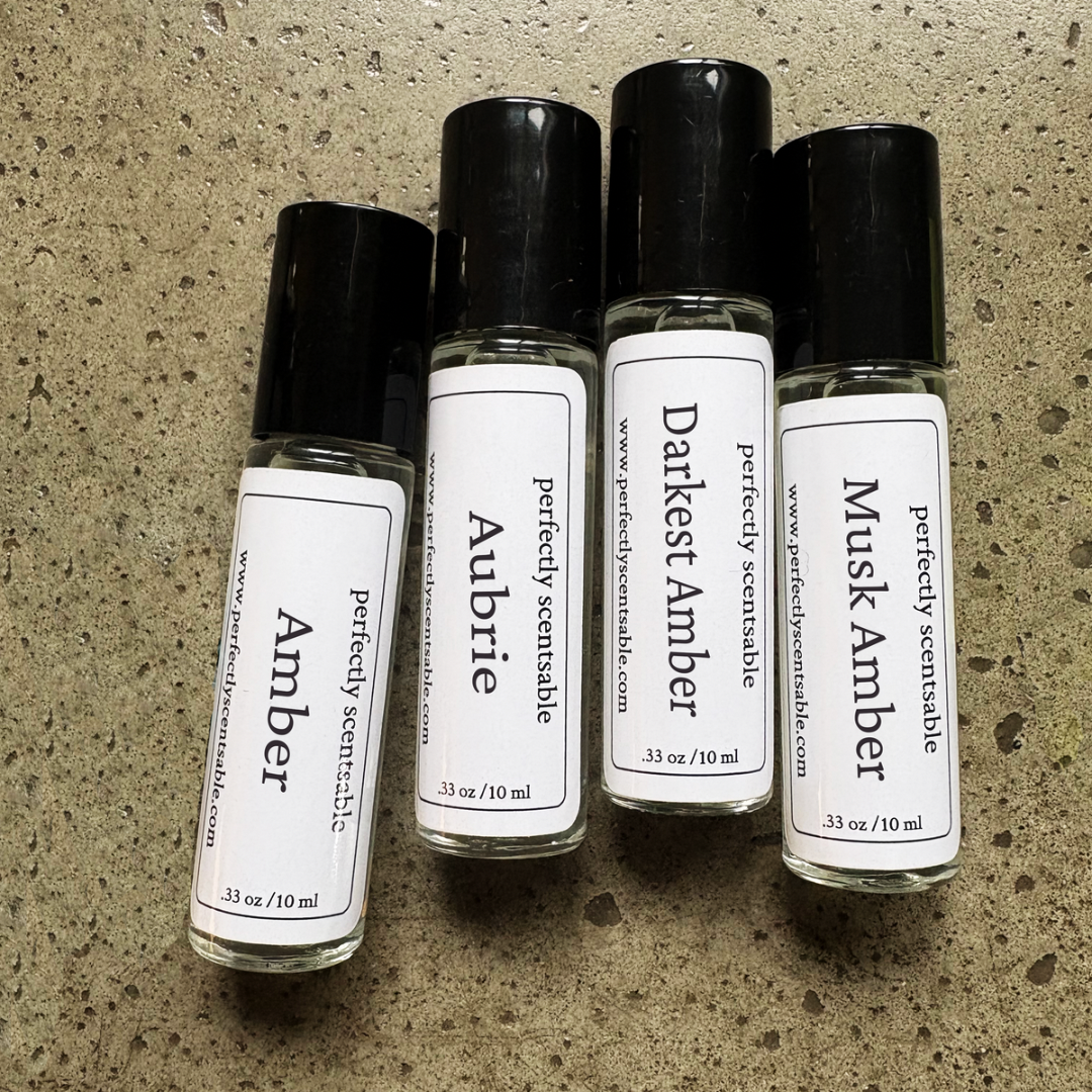 Set of four 10 ml (.33 oz) rollerball perfume oils by Perfectly Scentsable featuring Amber, Aubrie, Darkest Amber, Musk Amber displayed on a textured surface.
