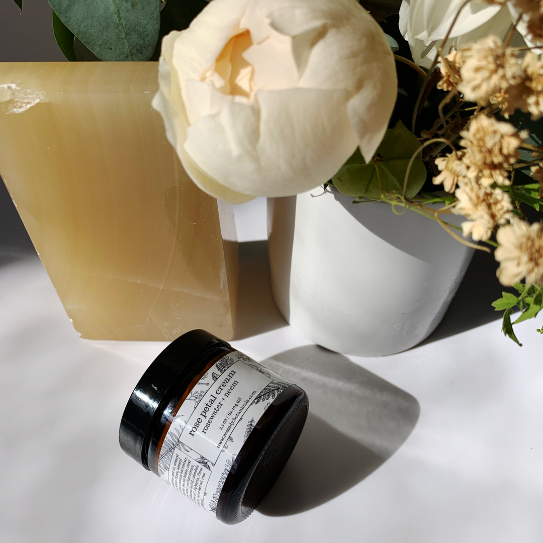 Top view of a bottle of Rose Water Cream beside orange bars, with an assortment of vibrant florals