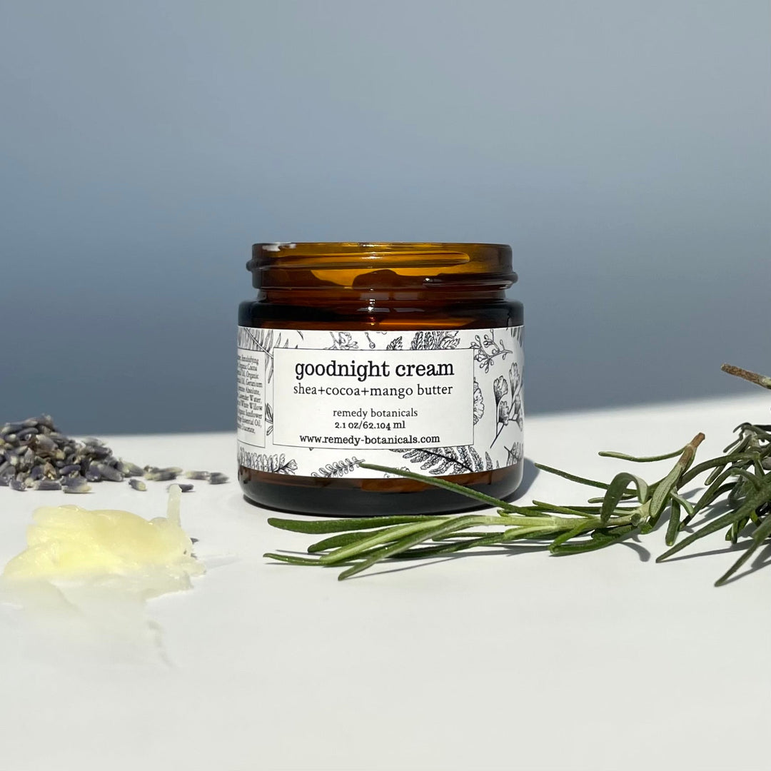 Amber jar of Remedy Botanicals Goodnight Cream with herbs and cream on a white surface.