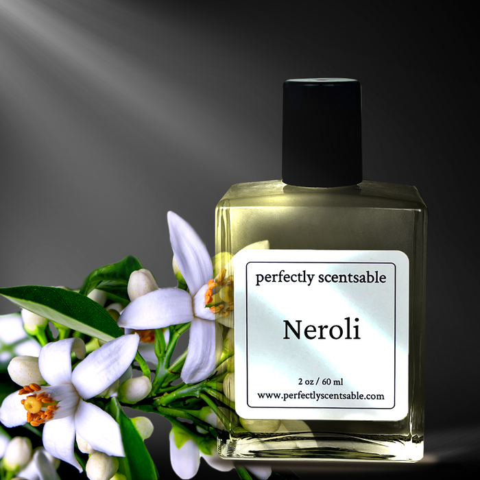 Perfectly Scentsable Neroli perfume oil, 2 oz/60 ml bottle with black cap beside orange blossoms under a soft spotlight on a dark background.