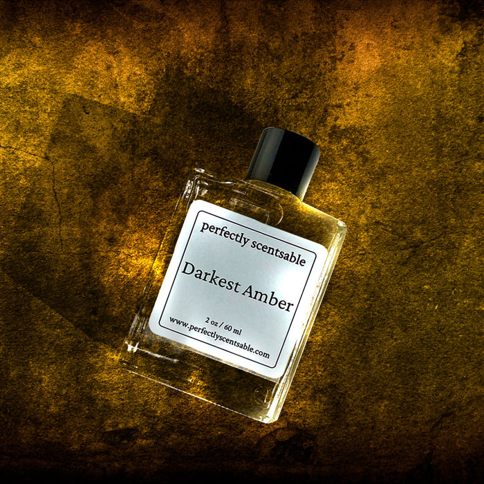 Perfectly Scentsable Darkest Amber perfume oil, 2 oz/60 ml square bottle with black cap, tilted on a textured golden-amber background.