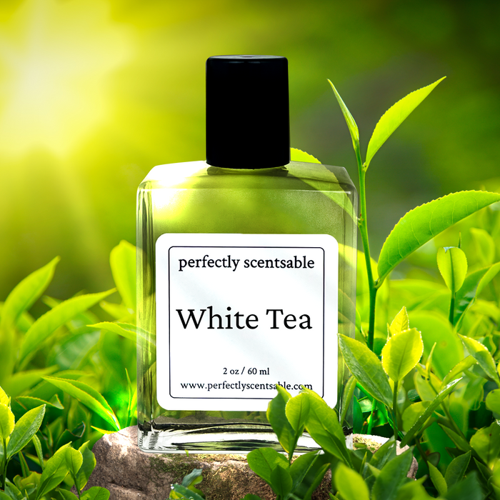 Perfectly Scentsable White Tea perfume oil bottle nestled among fresh tea leaves with warm sunlight.