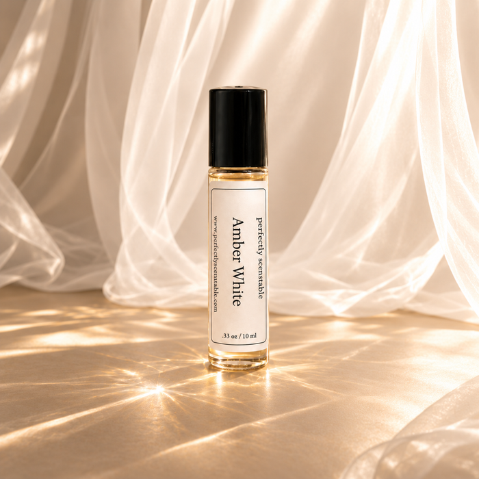 Amber White roll-on perfume bottle displayed against softly draped white fabric, illuminated by warm golden sunlight with delicate reflections and an elegant, airy atmosphere.