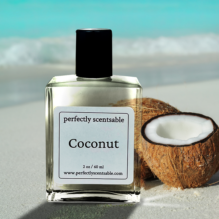 Coconut perfume oil by Perfectly Scentsable, 2 oz/60 ml bottle on sandy beach beside a halved coconut and turquoise water.