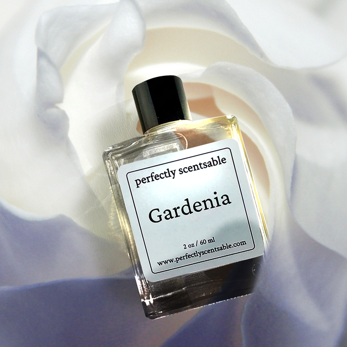 Perfectly Scentsable Gardenia perfume oil, 2 oz/60 ml square glass bottle with black cap, angled over a close-up white gardenia bloom background.