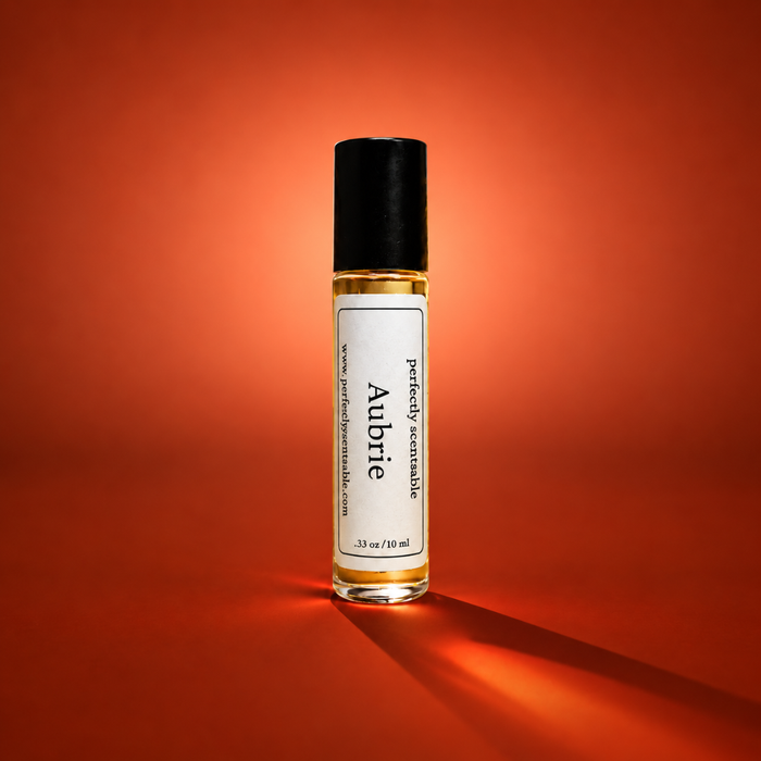 Aubrie roll-on perfume bottle centered against a rich burnt-orange background, illuminated by warm dramatic lighting with a long soft shadow extending across the surface.