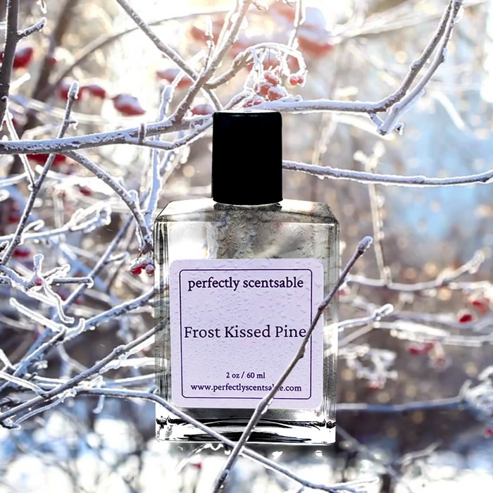 Frost Kissed Pine perfume oil, 2 oz/60 ml, dewy glass bottle set against sunlit branches coated in frost with red winter berries.