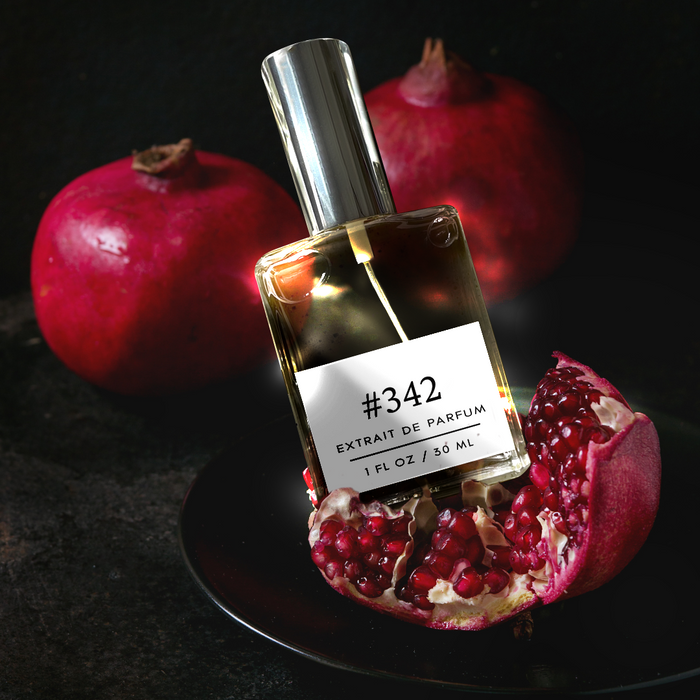 Perfectly Scentsable #342 extrait de parfum bottle resting on a plate with a cut pomegranate and whole pomegranates on a dark background