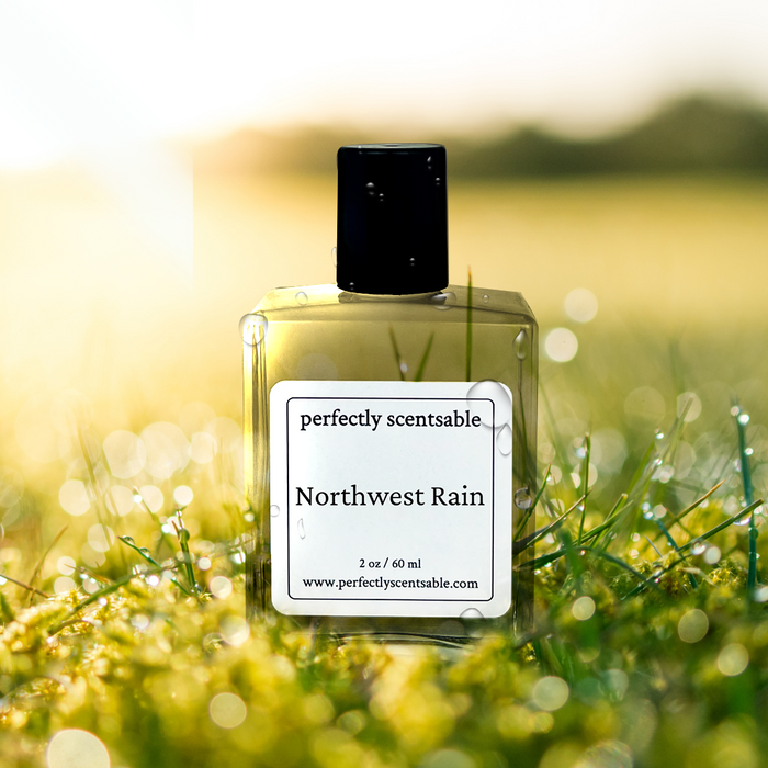 Perfectly Scentsable Northwest Rain perfume oil, 2 oz/60 ml square bottle with black cap on dewy grass at sunrise.