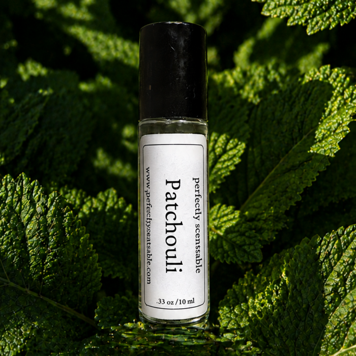 Patchouli roll-on perfume bottle nestled among lush, textured green leaves, highlighted by soft natural light against a deep green background.