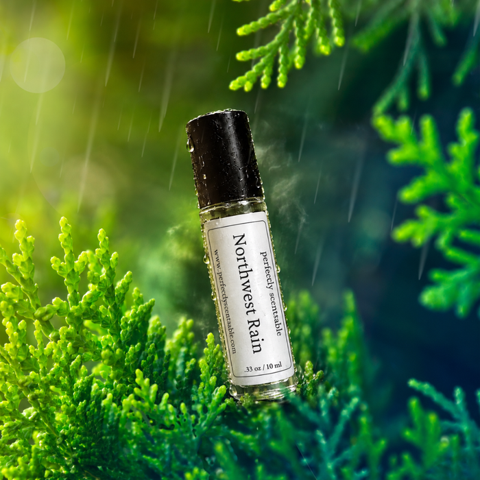 Northwest Rain roll-on perfume bottle covered in water droplets and nestled among lush green evergreen foliage, with falling rain and a misty green forest background.