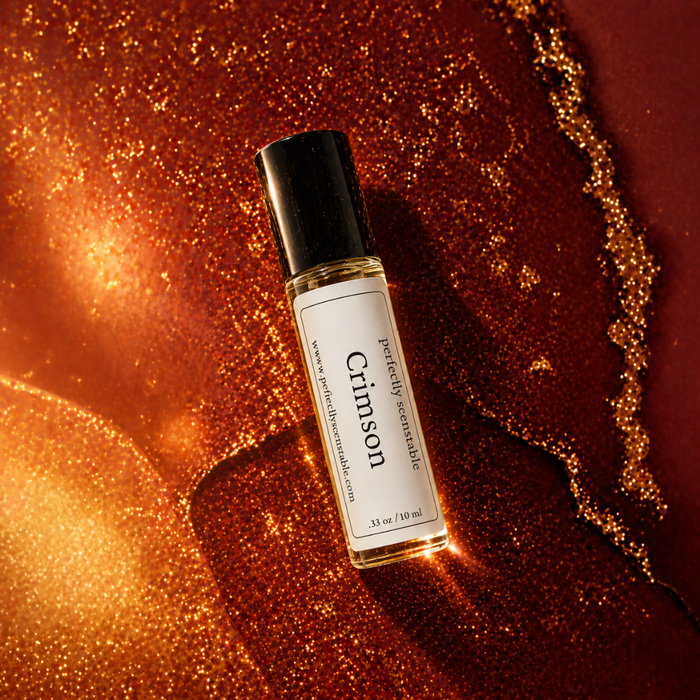Crimson roll-on perfume bottle displayed at an angle over a rich red and amber textured background, illuminated with warm golden highlights and sparkling metallic details.