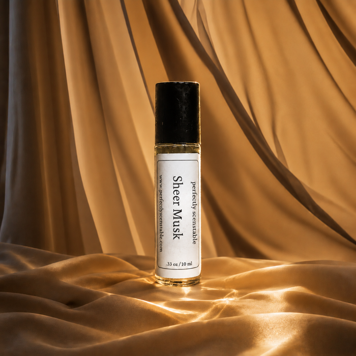 Sheer Musk roll-on perfume bottle standing on softly draped golden fabric, illuminated by warm light that creates elegant folds, shadows, and subtle reflections.