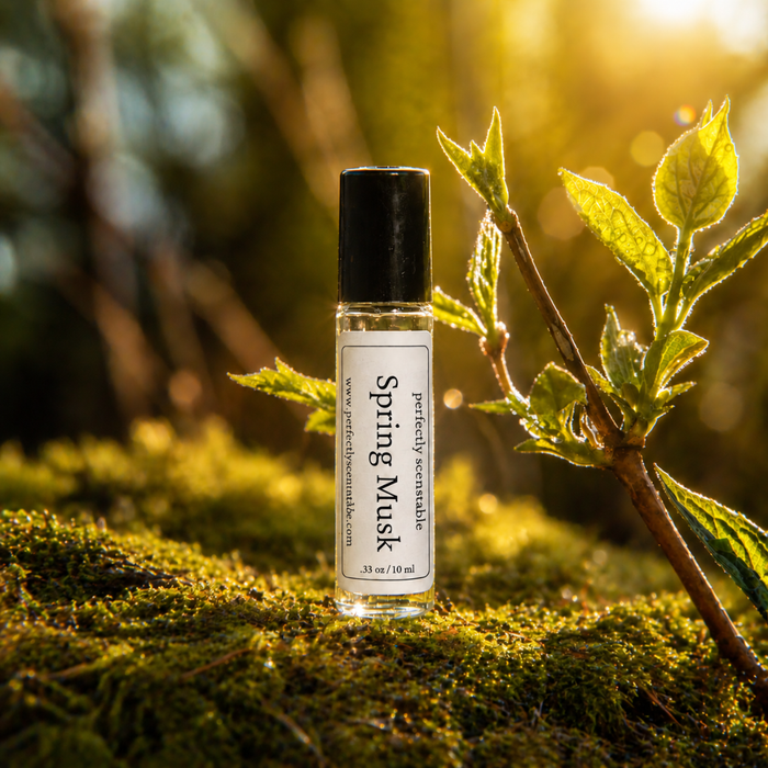 Spring Musk roll-on perfume bottle standing on lush green moss beside fresh budding leaves, illuminated by warm golden sunlight in a softly blurred natural setting.