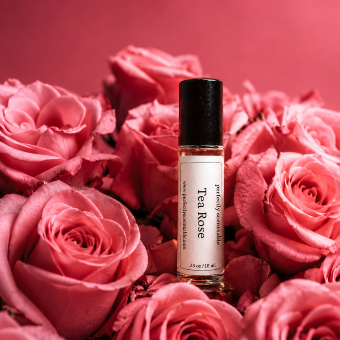 Perfectly Scentsable Tea Rose perfume oil bottle nestled among blooming pink roses on a soft rose-pink background