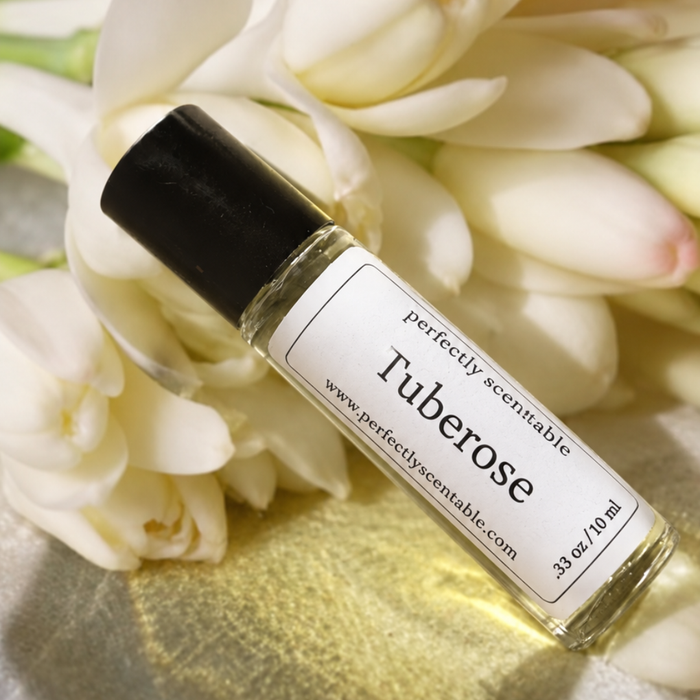 Tuberose roll-on perfume bottle resting diagonally among creamy white tuberose blossoms, softly illuminated with warm light and subtle golden reflections.
