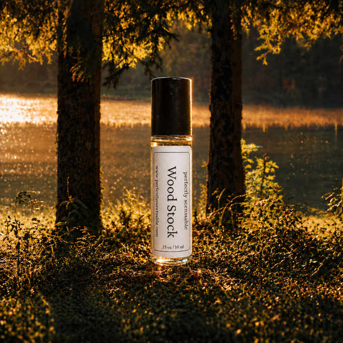 Wood Stock roll-on perfume bottle standing on the forest floor at golden hour, surrounded by tall trees and warm sunlight filtering through the woods.