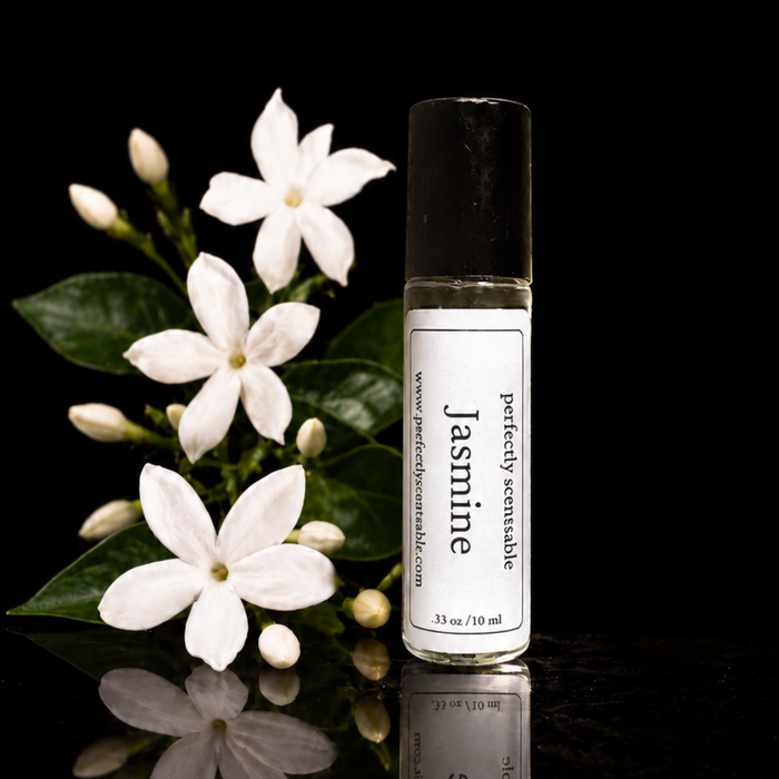 Jasmine roll-on perfume bottle displayed beside delicate white jasmine flowers and glossy green leaves against a deep black background, with subtle reflections on the surface.