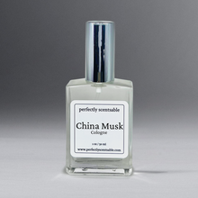 Load image into Gallery viewer, Clear 2 oz cologne bottle with silver cap against a grayish background.
