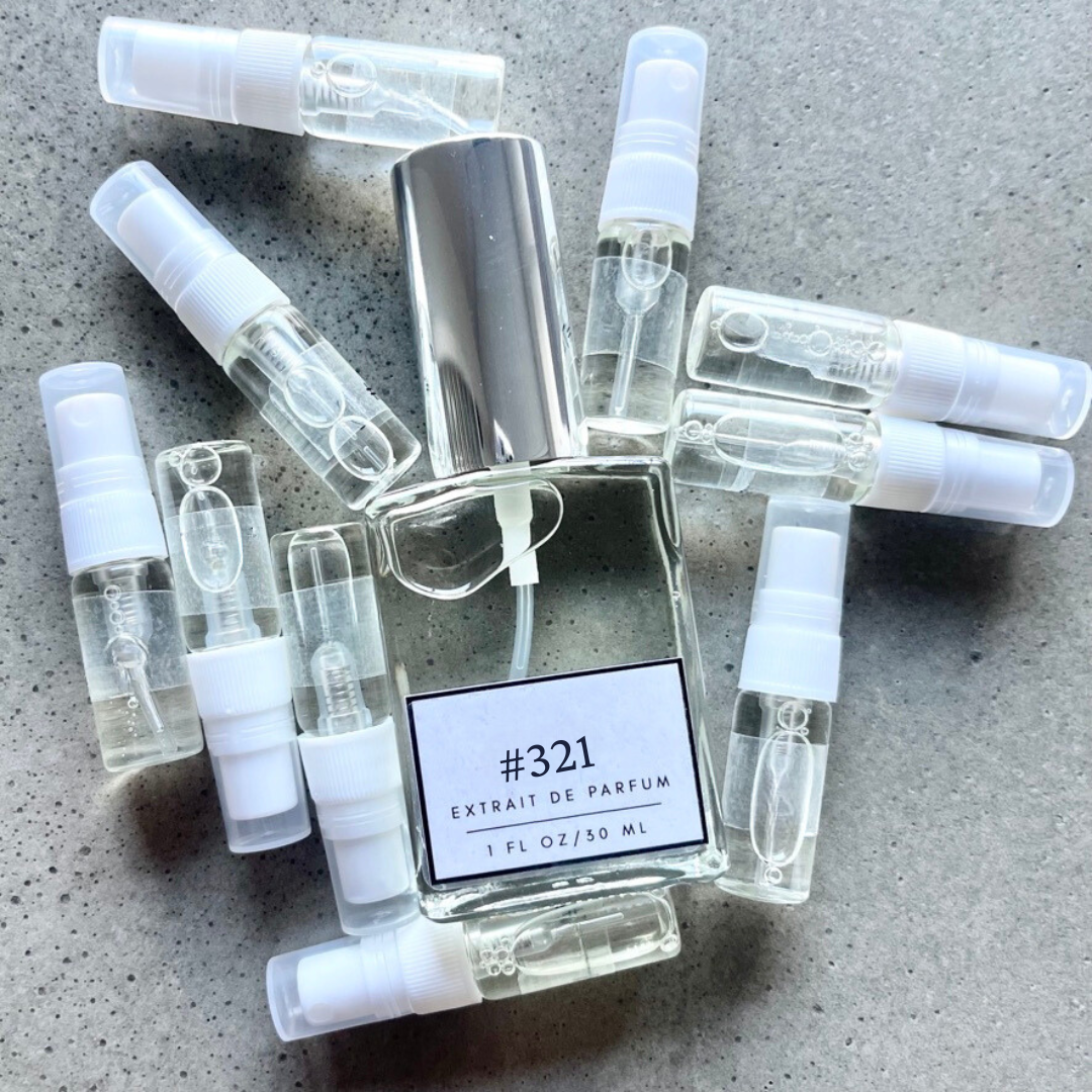 Clear bottle labeled with #321 Extrait De Parfum with silver cap, accompanied by 10 elegantly arranged sample bottles, resting on a marble surface.