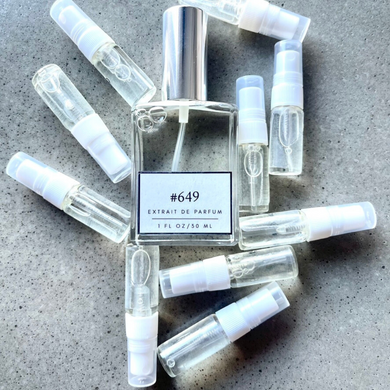 Clear bottle labeled with #649 Extrait De Parfum with silver cap, accompanied by 10 elegantly arranged sample bottles, resting on a marble surface.