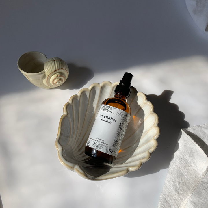 Top view of a bottle of Revitalize facial oil resting in a decorative pearl shell figurine, with a small seashell placed beside it, evoking a fresh, coastal vibe.