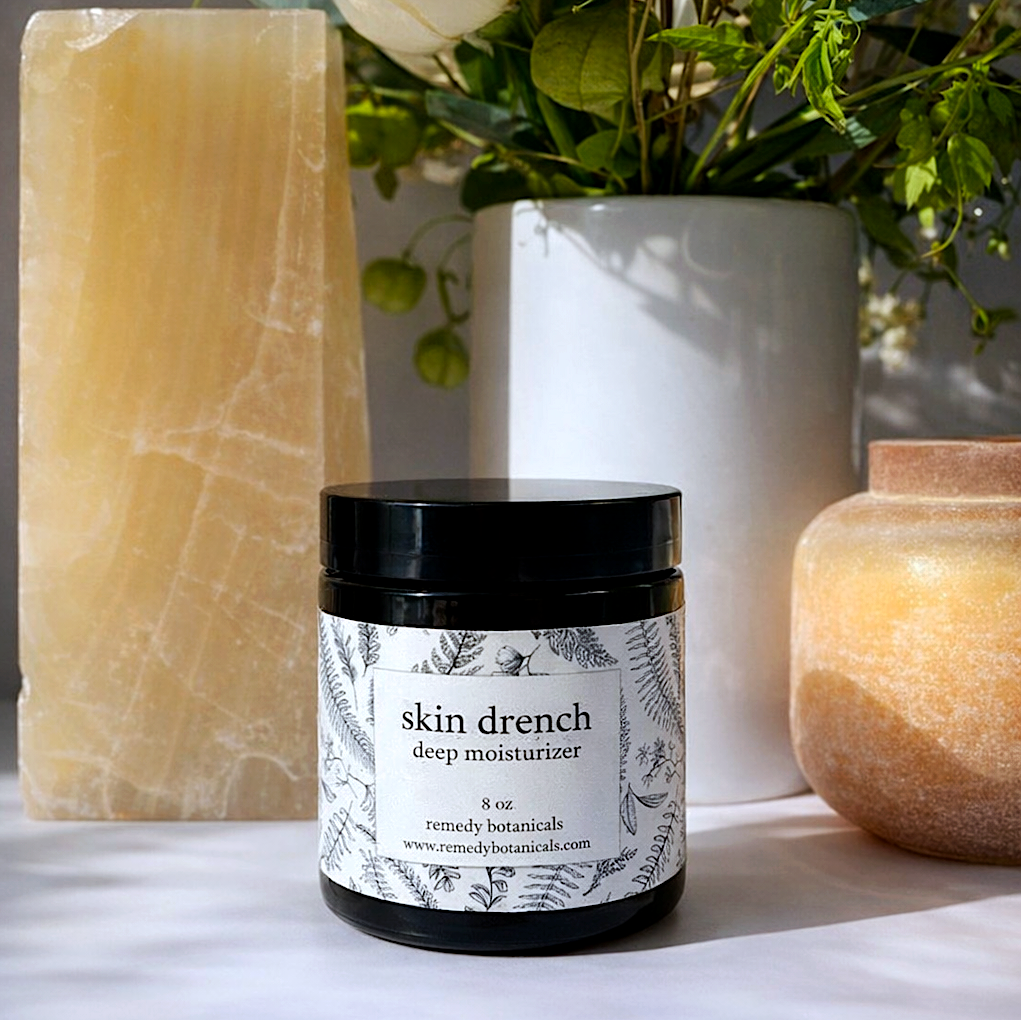 Jar of 'skin drench deep moisturizer' with decorative candles and flowers in the background