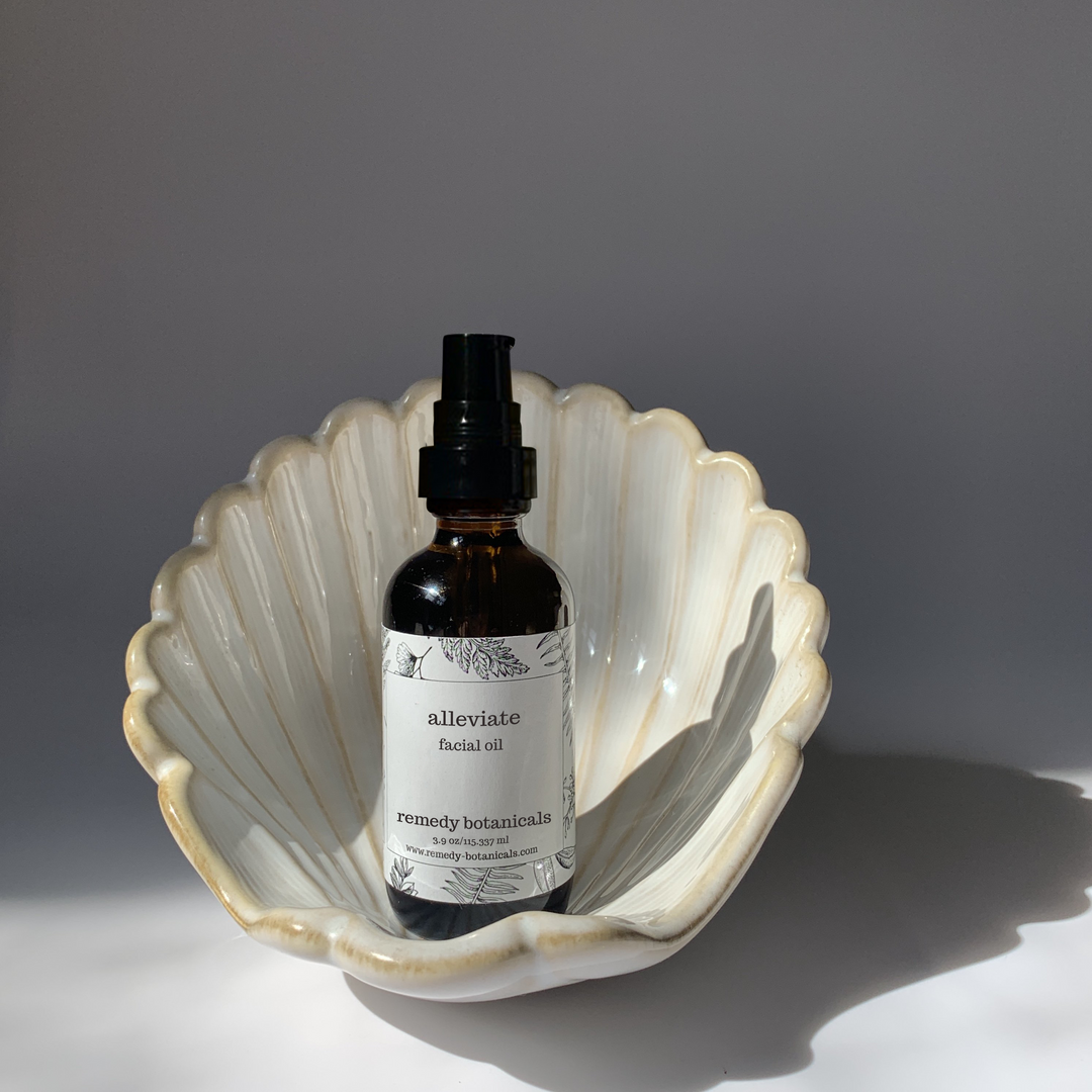 An Alleviate facial oil, standing on a pearl figurine on a gray blackground.