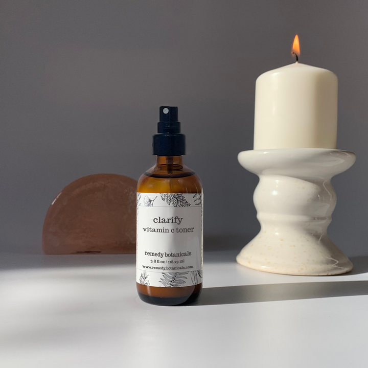 A clarify mist bottle standing beside a lighted candle with a gray background