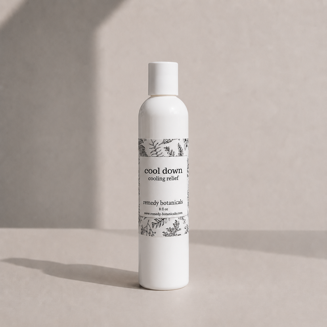 A white bottle of 'cool down cooling relief' by remedy botanicals stands on a light beige surface against a matching beige background with soft shadows.