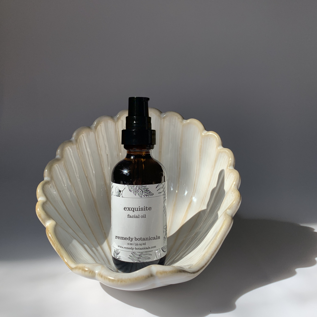 Bottle of Remedy Botanicals facial oil in a shell dish on a gray background