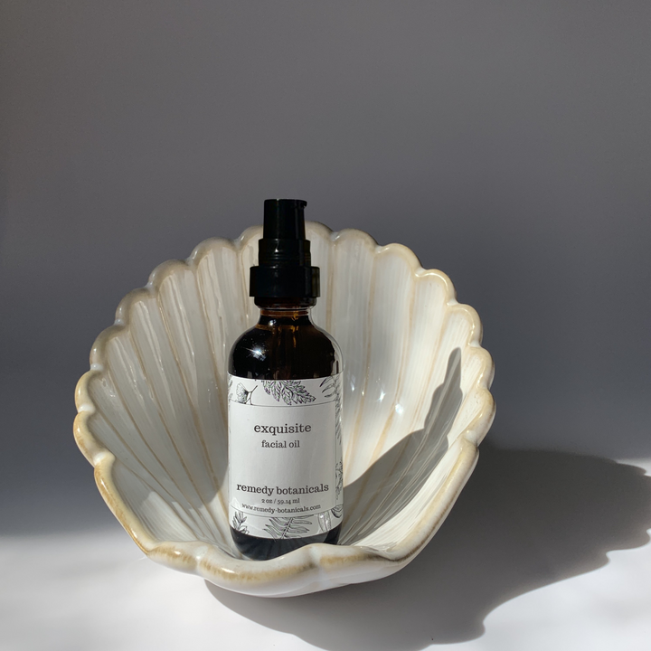 Bottle of Remedy Botanicals facial oil in a shell dish on a gray background