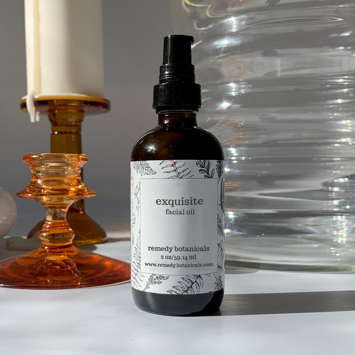 Bottle of 'exquisite facial oil' by remedy botanicals with a candle and glass container in the background.