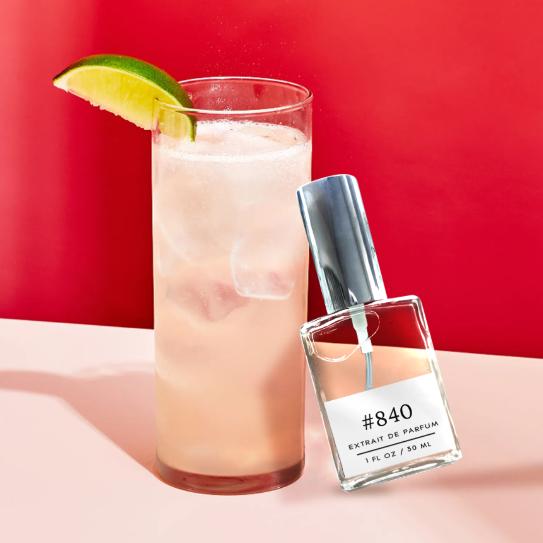 A 30 ml label for Formula 840 Moscow Mule by Juliette Has a Gun. The perfume bottle leans against a glass of Moscow Mule drink on a red background, resting on a creamy table. The label showcases the citrusy, woody, and aromatic fragrance for women, evoking the essence of luxury and sophistication.